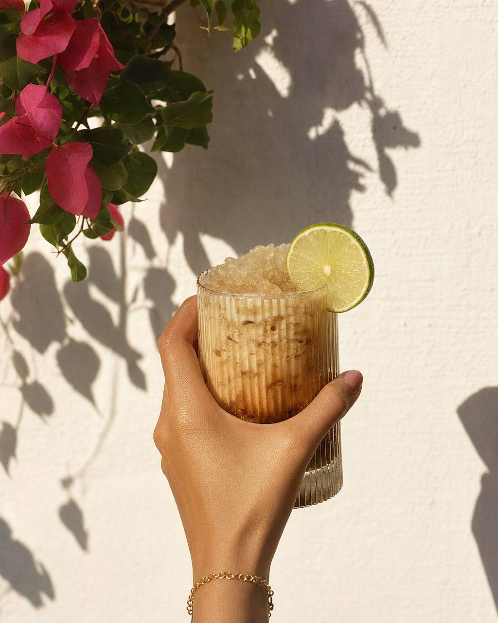 A hand holding a creamy cola soda against a white plaster wall